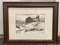 Framed winter landscape painting with barn and silos covered in snow.