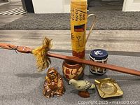 Overview of the trinket lot showing all items on a table: Buddha figurine, vase, drum, wooden bird, smoking pipe with feather, brass ashtray.