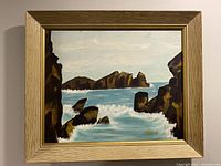 Full view of the framed seascape painting depicting ocean waves crashing on rocky cliffs.