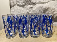 Set of 8 vintage drinking glasses with blue and gold diamond and dot geometric pattern on clear glass against a stone background.