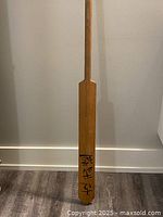 Full length wooden paddle showing natural wood and signature near blade.