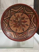 Top view of a round pottery plate with central flower design and star-shaped geometric patterns in earthy colors.