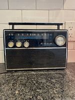 Front and angled view of the vintage Koyo solid state AM/FM radio showing front panel controls, tuning dial, carry handle, and power cord.