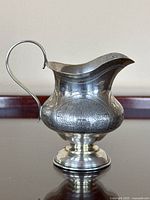 Side profile of silver creamer showing body shape and handle