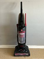 Front view of the Hoover WindTunnel vacuum cleaner with red and black body, attached hose, and crevice tool.