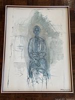 Full view of the lithograph showing the seated female figure in shades of gray within a walnut frame on a wood floor.