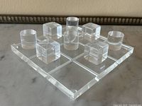 Close-up front view of the Lucite game board loaded with five cube pieces and four cylinder pieces arranged on the board.