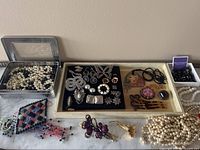 Overview of trays showing mixed faux pearl necklaces, brooches, earrings, hair accessories and beaded pendant