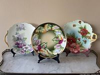 Lot of three hand painted decorative floral porcelain plates shown together on stands.