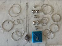 Overview photo showing all items including multiple pairs of hoop earrings, clip-on earrings, rings, and necklaces laid flat on a marble surface