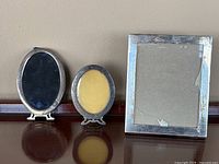 All three picture frames displayed together: two smaller oval frames with tarnish and damage, and one rectangular Gorham frame with tarnished silver surface.