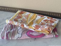 Folded view showing two folded scarves, one with warm earth tones and the other pink and grey colors