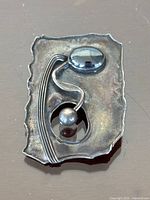 Top angled view of abstract modernist sterling silver brooch pendant showing textured rectangular shape with silver ball and polished oval stone connected by curved wire.