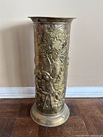 Front view of the embossed brass umbrella stand showing the full embossed scene and flared rim.