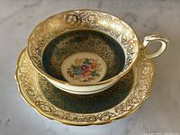 Top angled view of teacup and saucer showing detailed floral center and intricate gold lace pattern.