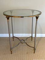 Side view of the vintage round metal and glass end table showing its slender legs, glass top, and decorative gold-tone accents.