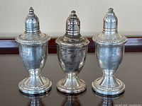 Photo showing all three vintage sterling silver salt and pepper shakers side by side on a dark wood surface.