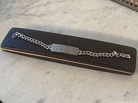 Sterling silver ID bracelet displayed on a closed black presentation box on a marble surface.