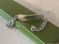Close-up front view of the sterling silver ID bracelet showing the curb chain and blank half matte plate on a green textured surface.