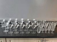 Wide view of all glasses set on a counter showing an assortment of champagne coupes, wine glasses, cordial glasses and tumblers.