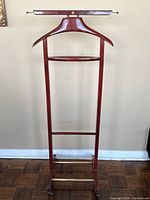 Full front view of the vintage wooden valet stand showing the hanger bar, jacket hanger, middle shelf, and base with casters.