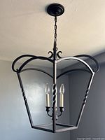 Black wrought iron hanging light fixture with three candle-style bulbs hung from black chain, shown unlit.
