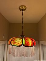 Hanging stained glass lamp shown from a distance while lit, hanging from ceiling chain.