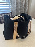 Black tote bag with gold-colored textured vertical stripes and black handles on a white table.