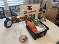 Full view of bar accessories on table including Moosehead Pale Ale sign, large martini glass, multiple bottles, shot glasses, and moose head decor.