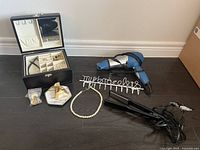 Photo of jewelry box and all hair tools set on floor, showing jewelry box, necklace, bracelet holder, gold pouch, hair dryer, and hair straightener.