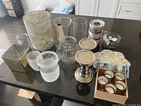 Top view showing various candle holders, decorative vases, metal candlesticks, box of tealights, and small candle accessories arranged on a table.