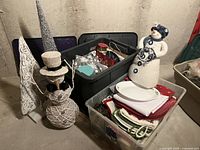 Photo shows various Christmas decor including snowman figurines, linens, and tree decor in plastic bins