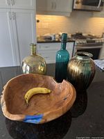Overview of wooden bowl with banana inside and three vases behind it on a light kitchen counter