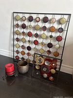 Full lot showing large metal wall art, smaller metal art, vase, planter, candleholder and candle on dark floor against white wall.