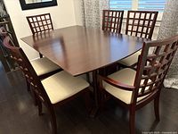 Full view of the rectangular dining table with leaf insert, surrounded by six chairs, all made of dark wood with beige padded seats.