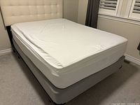 Full view of double bed setup showing memory foam topper with mattress protector on a grey box spring and metal frame, under ivory headboard