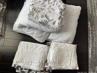 Stack of linens including a white quilted mattress protector, floral printed duvet cover, pillowcases with dot pattern, and white sheet.