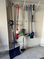Full view of all garden and cleaning tools hanging against wall including snow shovel, rakes, edgers, mop, and broom.