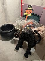 Photo showing the black plastic cauldron, black cat figure made from wire and fibers, Halloween pumpkin witch hat sign, and part of a beige table cloth with leaf patterns.