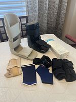 Overview of all items on table including Aircast ankle brace, black Air Walker boot, sleeping brace, tensor bands, and ankle supports