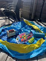 Wide view showing deflated blue and yellow inflatable pool with blue toy truck, unopened fishing toy set, green water squirter, and pogo jumper