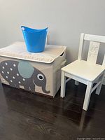 Three items: fabric toy storage chest with elephant design, white kids chair, blue plastic bin atop the chest