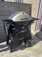 Full view of Weber BBQ grill showing black stand, gray lid, side shelves, and wheels.