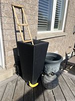 Tall black woven planter with wooden trellis held upright for scale, with a banana for size comparison, plus round planter and outdoor lantern visible on deck.