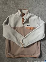 Full view of Patagonia fleece quarter zip pullover laid flat showing cream upper and sleeves and light brown lower body with salmon trim and snap buttons.