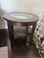 Side view of round wood end table with glass inset and lower wood shelf.