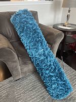 View of rolled blue shag rug with thick plush fibers, showing overall length and texture.