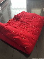 Red single bed sized quilt laid out folded on floor showing size and texture.