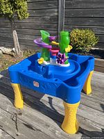 Full side view of Step2 water table featuring removable green spiral slide, purple funnel, and yellow water wheels on a blue basin with yellow legs.