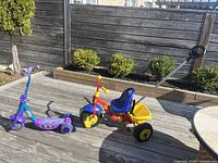Purple toddler three-wheel scooter and Kettler toddler tricycle with yellow bucket on deck.